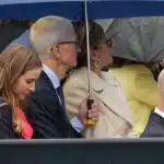 Tim Cook sitting with others under umbrellas in the rain