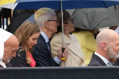 Tim Cook sitting with others under umbrellas in the rain