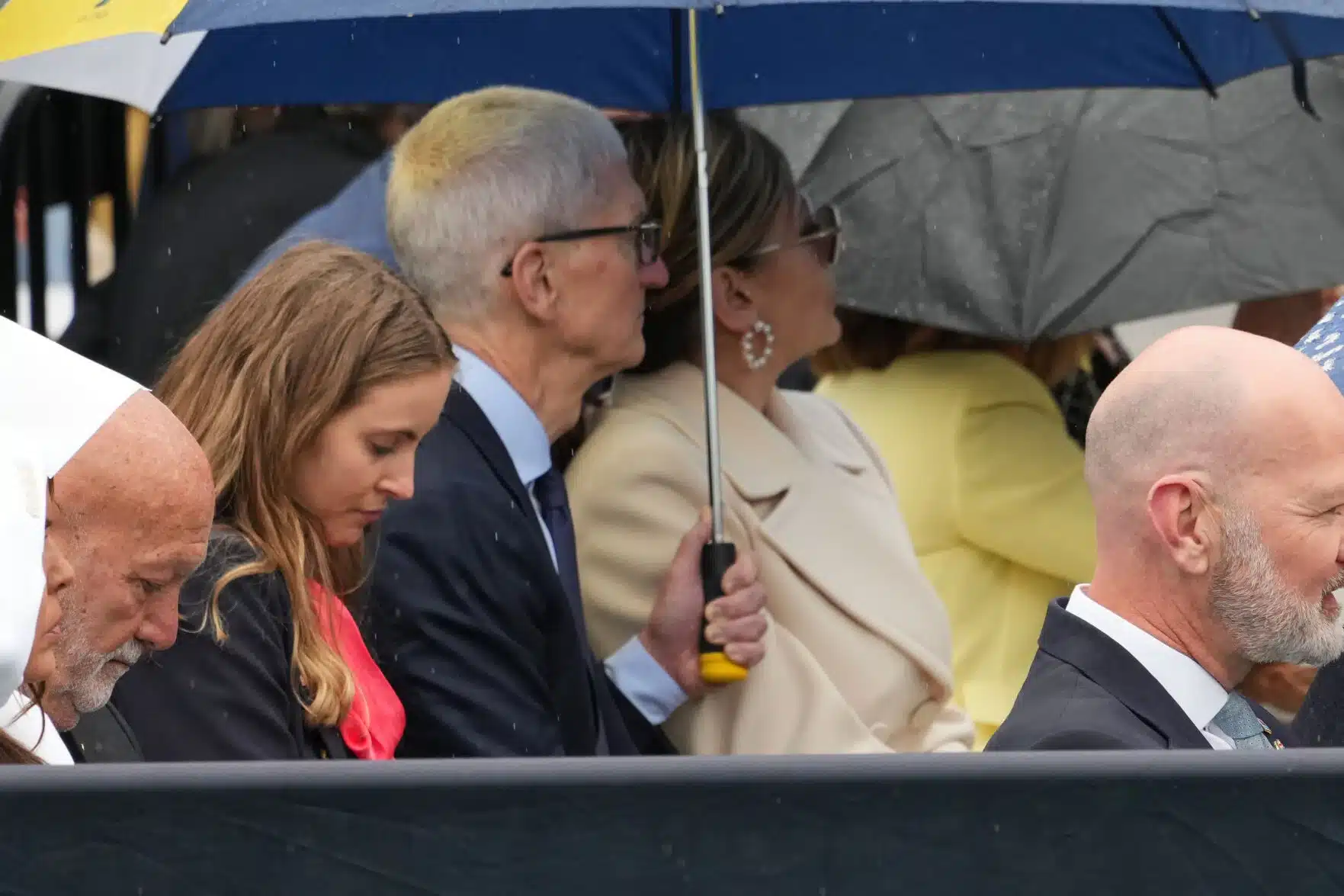 Tim Cook sitting with others under umbrellas in the rain
