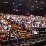 Large audience seated inside a modern movie theater auditorium.