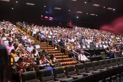 Large audience seated inside a modern movie theater auditorium.