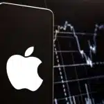 Apple logo on smartphone with stock market chart background.