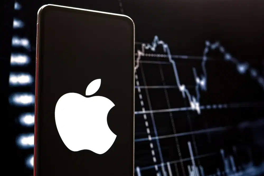 Apple logo on smartphone with stock market chart background.