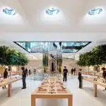 Interior of an Apple Store with product display tables and customers browsing.