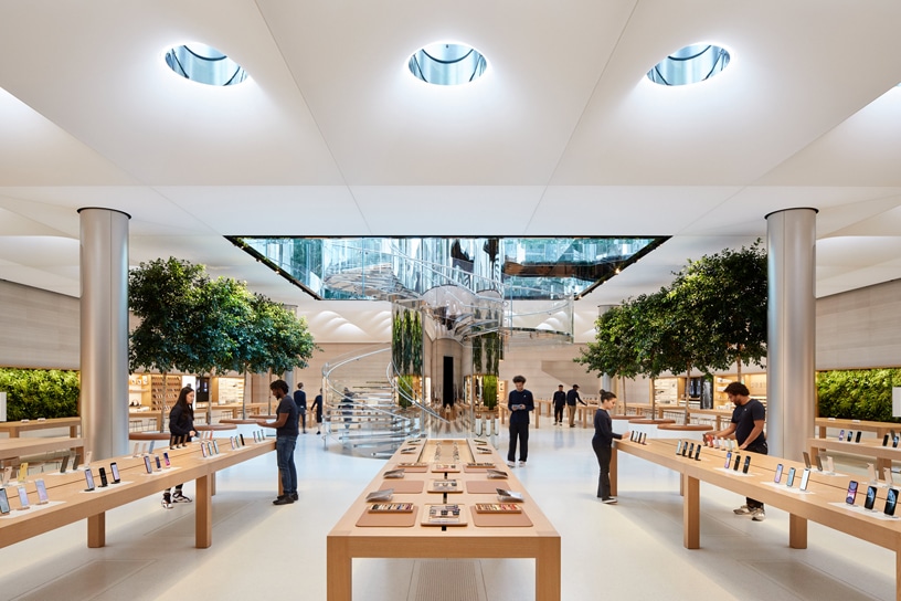 Interior of an Apple Store with product display tables and customers browsing.