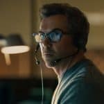 Patrick Brammall wearing a headset in a dimly lit office setting.