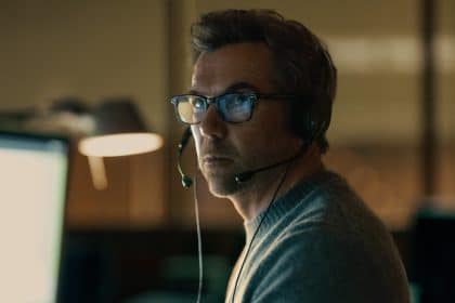 Patrick Brammall wearing a headset in a dimly lit office setting.