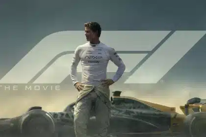 Race driver standing beside Formula 1 car in movie scene.