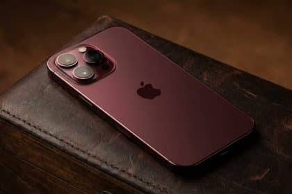 Dark red iPhone with a triple camera setup resting on a leather surface.