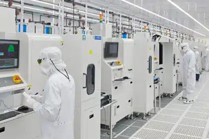 Workers in cleanroom suits operating machines in a high-tech manufacturing facility.