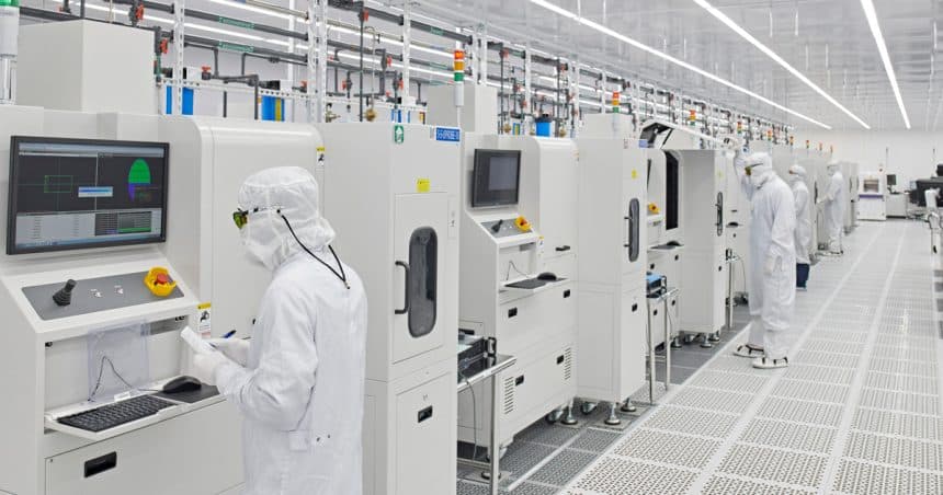 Workers in cleanroom suits operating machines in a high-tech manufacturing facility.