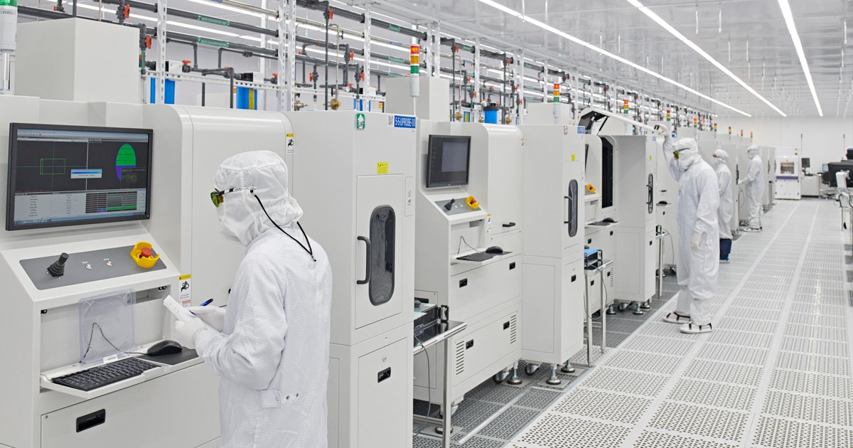 Workers in cleanroom suits operating machines in a high-tech manufacturing facility.