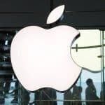 Apple logo displayed inside an Apple Store with people in the background.