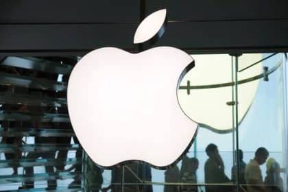Apple logo displayed inside an Apple Store with people in the background.