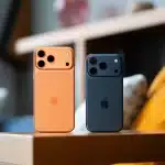 Two iPhone 17 Pro Max models in orange and blue standing on a table.