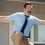Ted Lasso celebrates with his arms raised and a joyful expression.