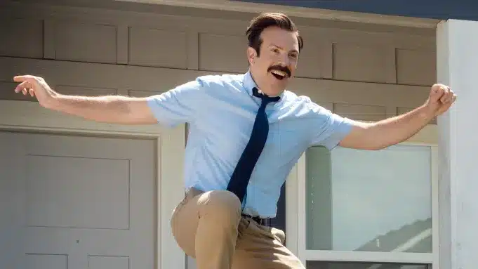 Ted Lasso celebrates with his arms raised and a joyful expression.