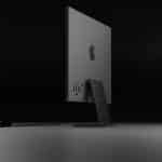 Rear view of a sleek black Apple iMac with a matching keyboard and mouse on a dark background.