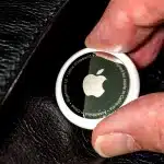 Close-up of an Apple AirTag held between two fingers.