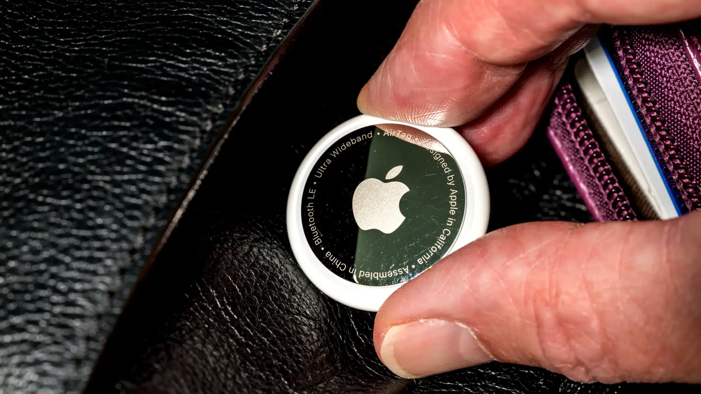 Close-up of an Apple AirTag held between two fingers.
