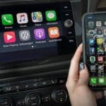 Apple CarPlay displayed on a car dashboard beside an iPhone.