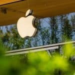 Apple logo displayed outside an Apple Store, reflecting trees and greenery.