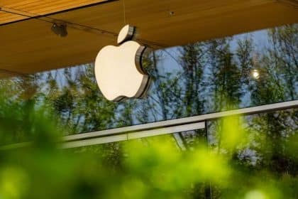 Apple logo displayed outside an Apple Store, reflecting trees and greenery.