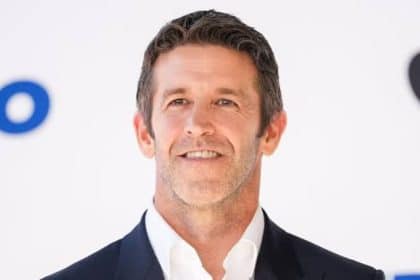 Apple executive smiling in a dark suit against a white background.