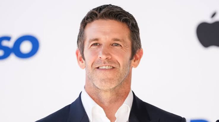 Apple executive smiling in a dark suit against a white background.