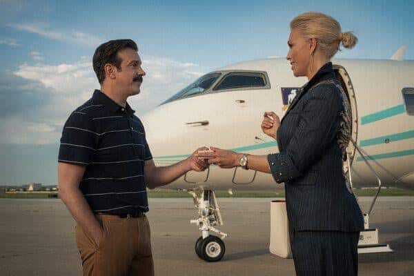Ted Lasso and a woman exchange a handshake beside a private jet.