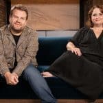 Two smiling people sitting together on a blue sofa.