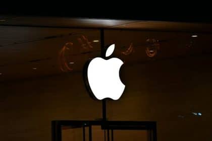 Illuminated white Apple logo on a dark storefront at night.