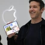 Apple executive smiling while holding an unfolded iPhone Duo in front of the Apple logo.