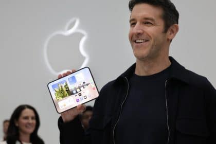 Apple executive smiling while holding an unfolded iPhone Duo in front of the Apple logo.