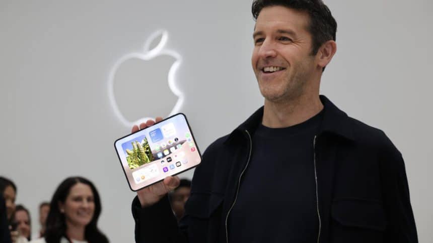 Apple executive smiling while holding an unfolded iPhone Duo in front of the Apple logo.