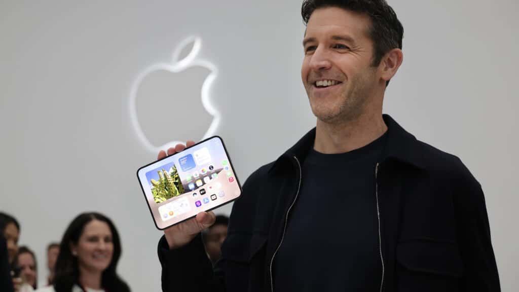 Apple executive smiling while holding an unfolded iPhone Duo in front of the Apple logo.